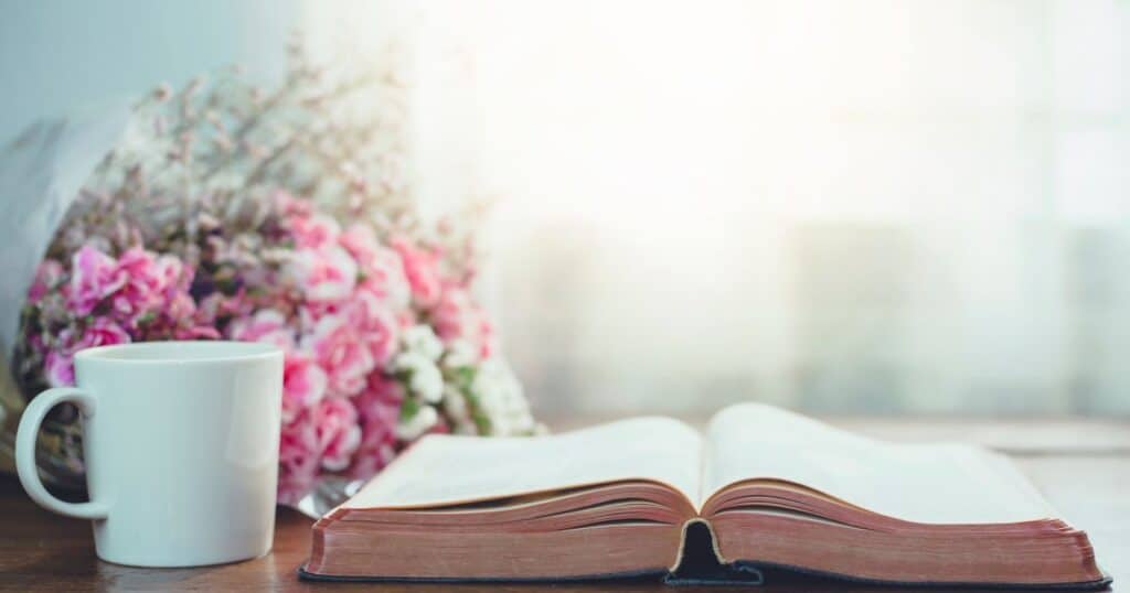 decorative picture of a coffee mug and a bible sitting on a desk by a window