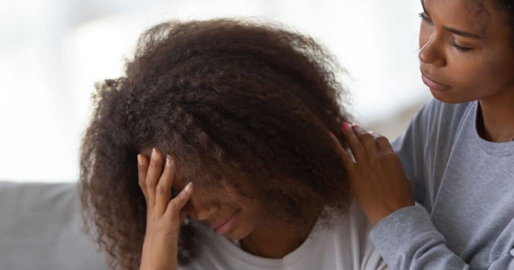 woman standing consoling another woman sitting with head buried in her hands