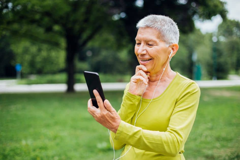 older woman looking at phone wearing earbuds